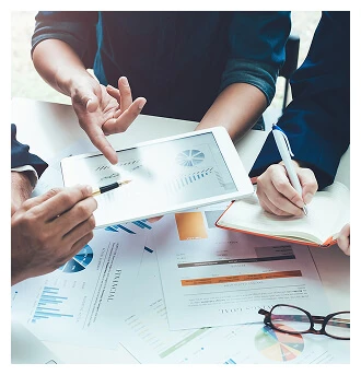 A group of business people engaged with a tablet, with papers and pens scattered around them on a desk.